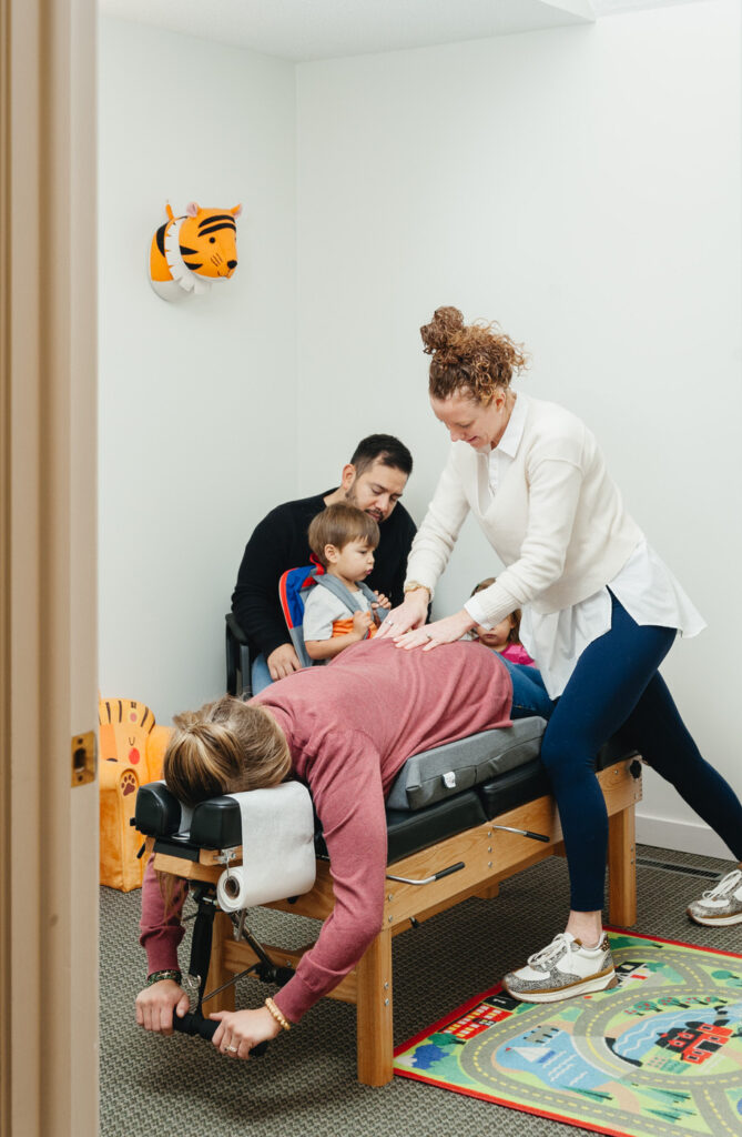 Dr. Kate Antoniotti adjusting a mother's back while the woman's husband and two young children sit in the room observing